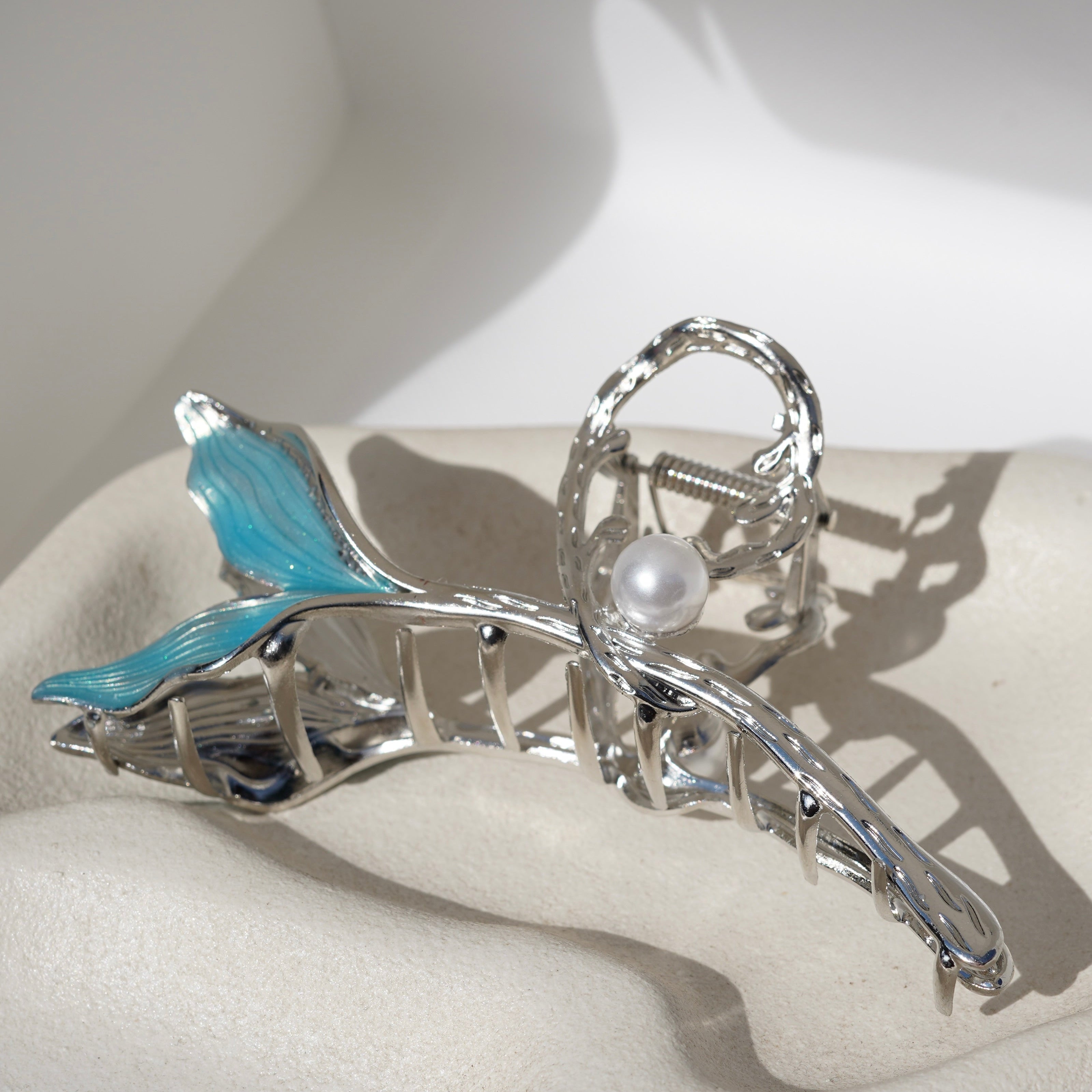 A silver and blue hair clip with a pearl embellishment, displayed on a white cloth.