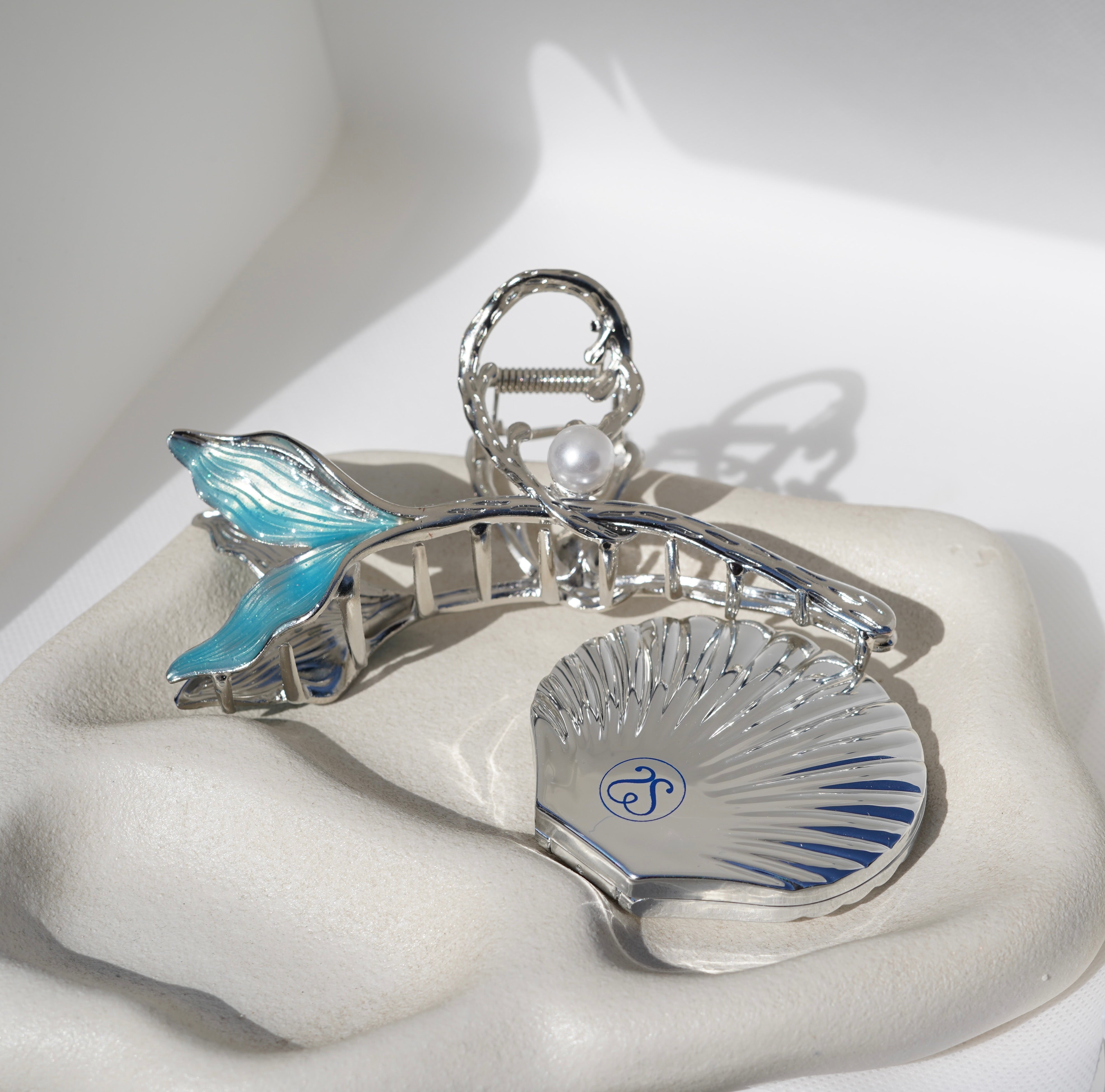 A silver hair clip with blue accents and a shell-shaped compact mirror.