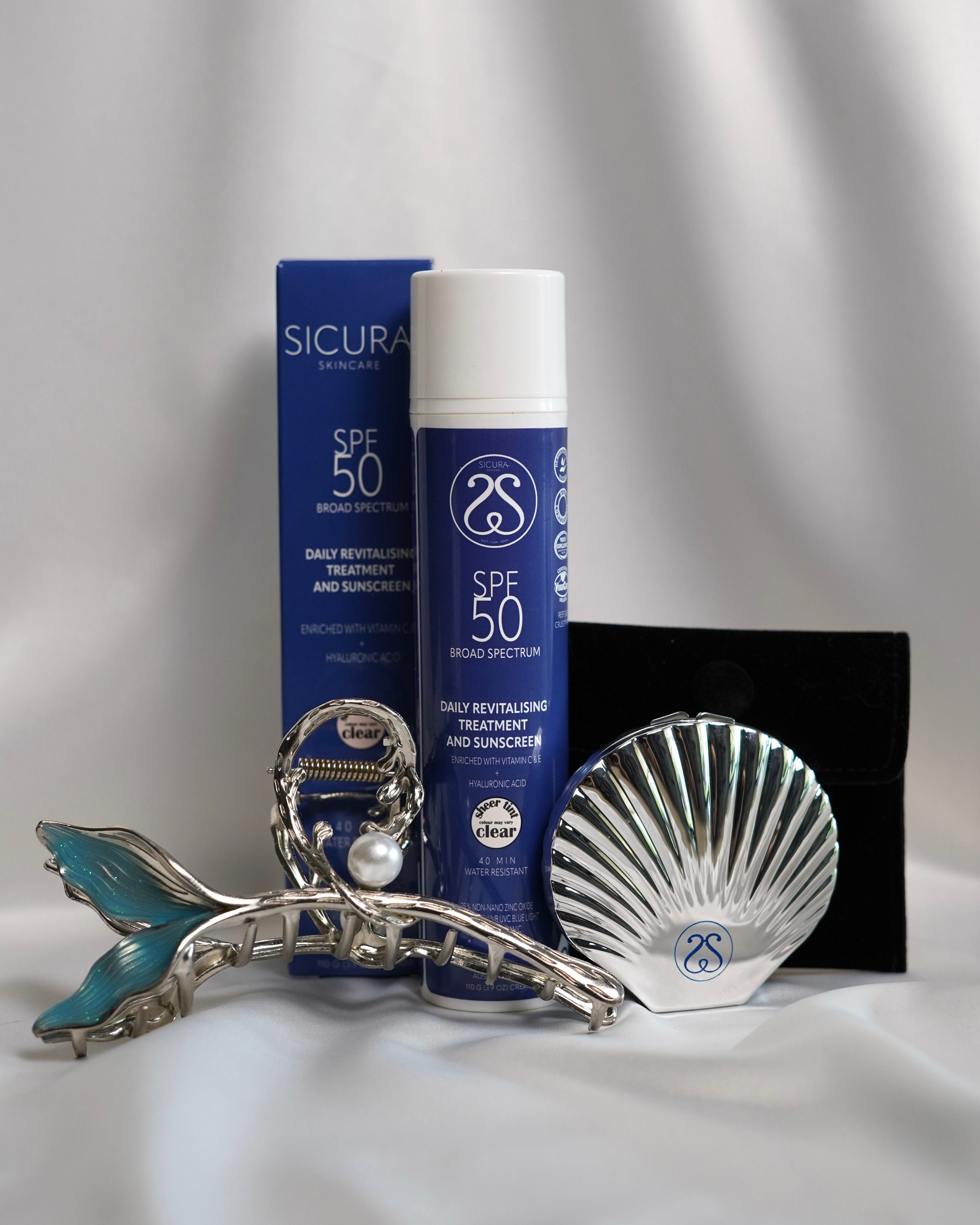 A Sicura skincare product trio, including a sunscreen, facial mist, packaged in a blue box with a decorative seashell.