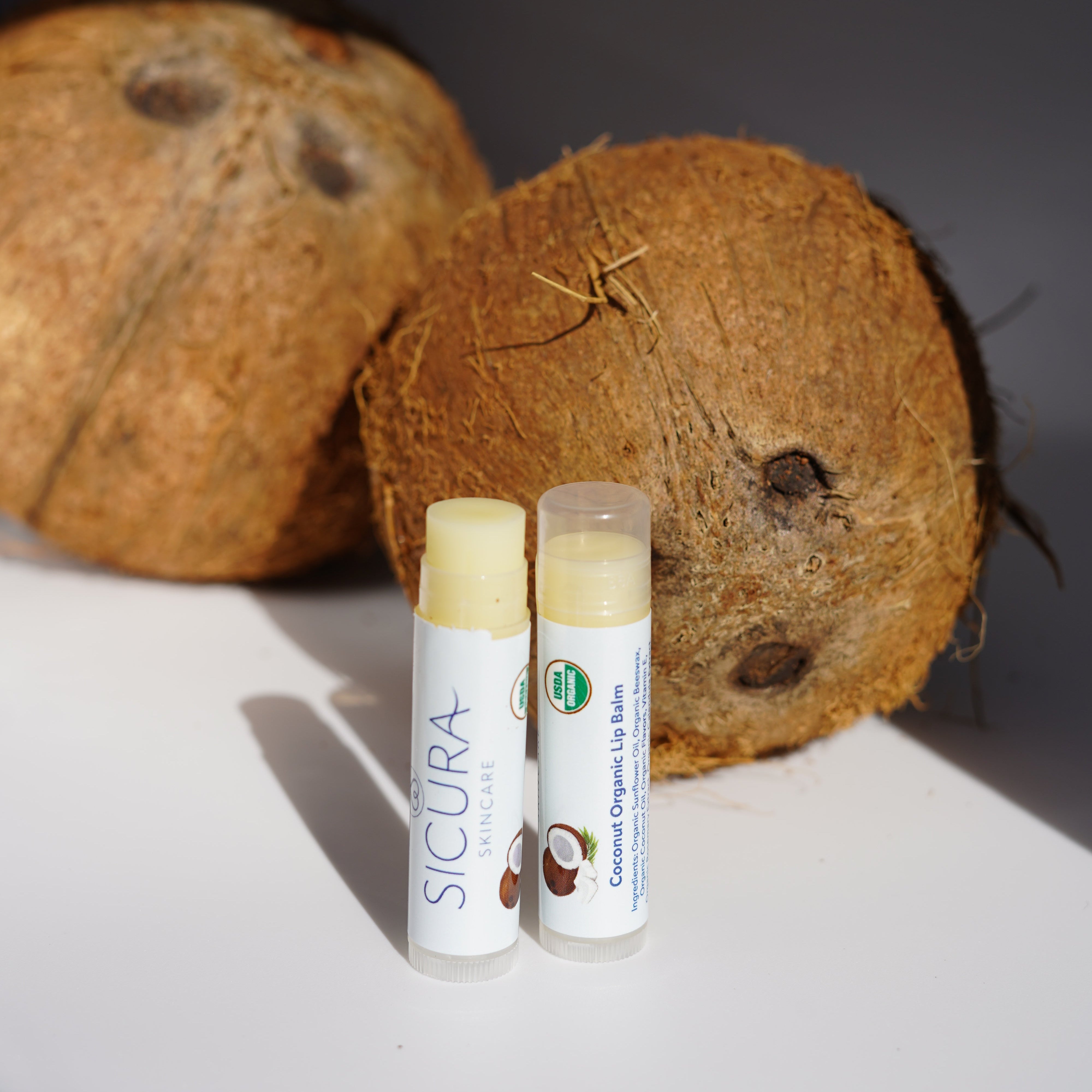 Two lip balms on a coconut with a dark background