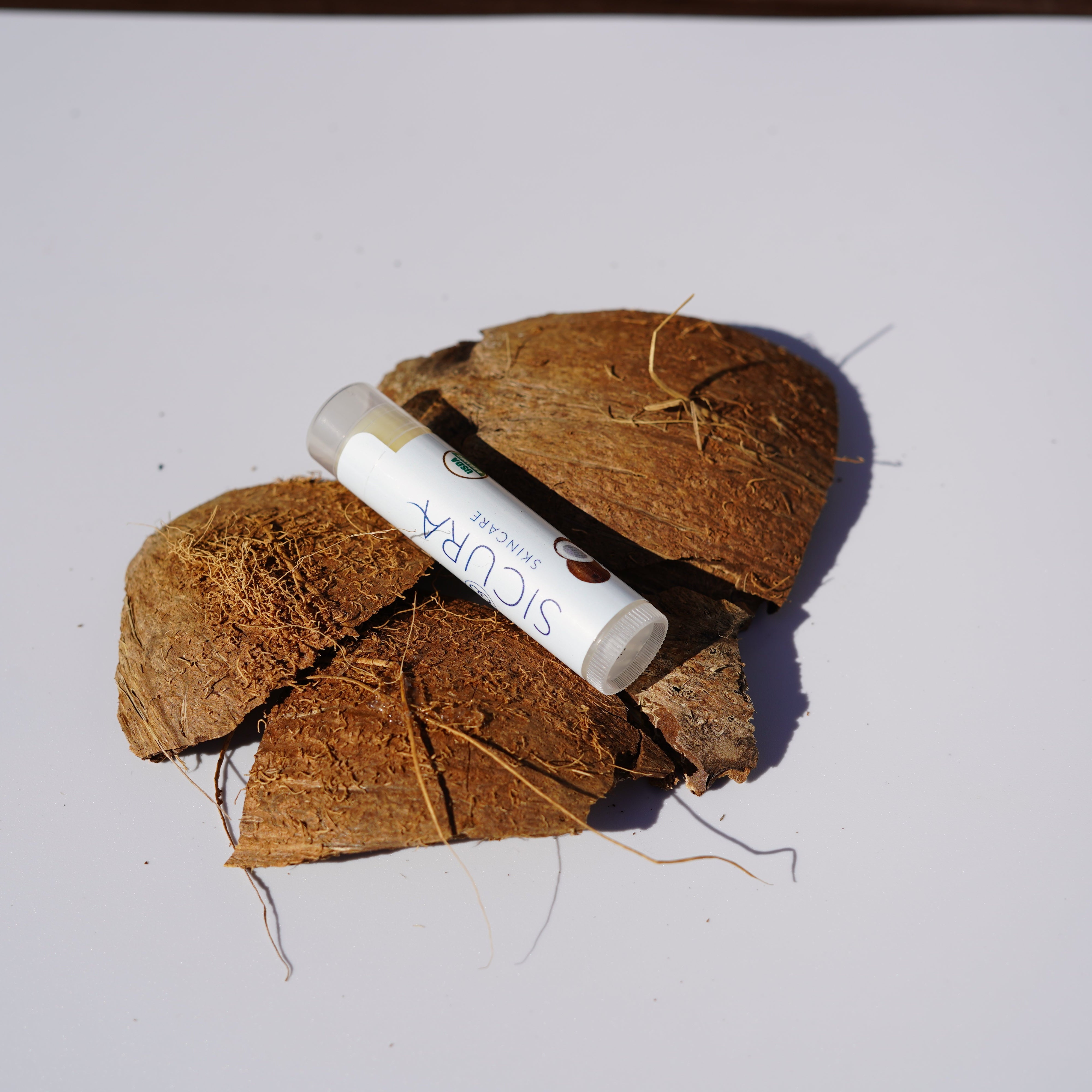 Coconut shell with a small container labeled 'SICURA' on a white background