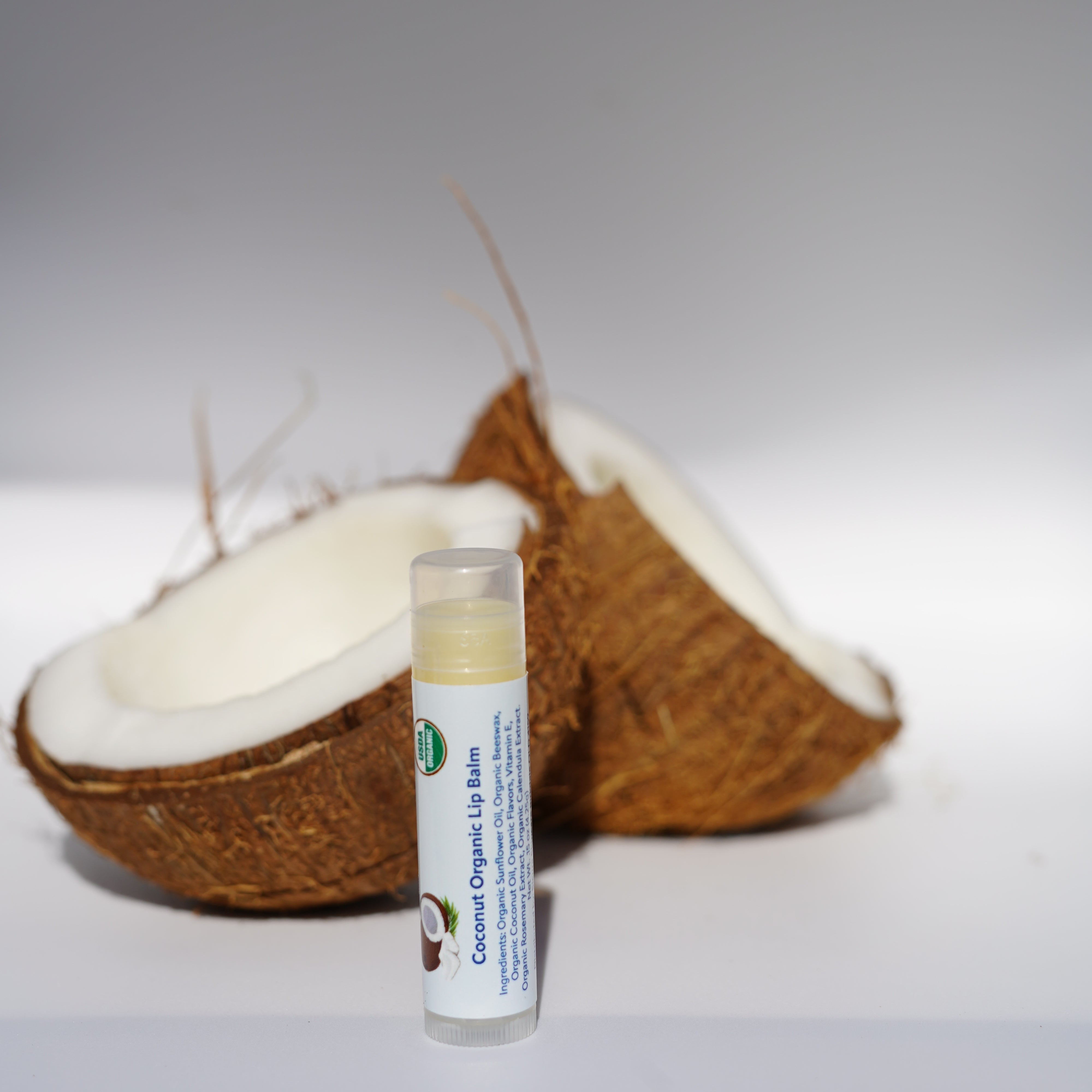 Coconut Organic Lip Balm on a half-cut coconut against a white background