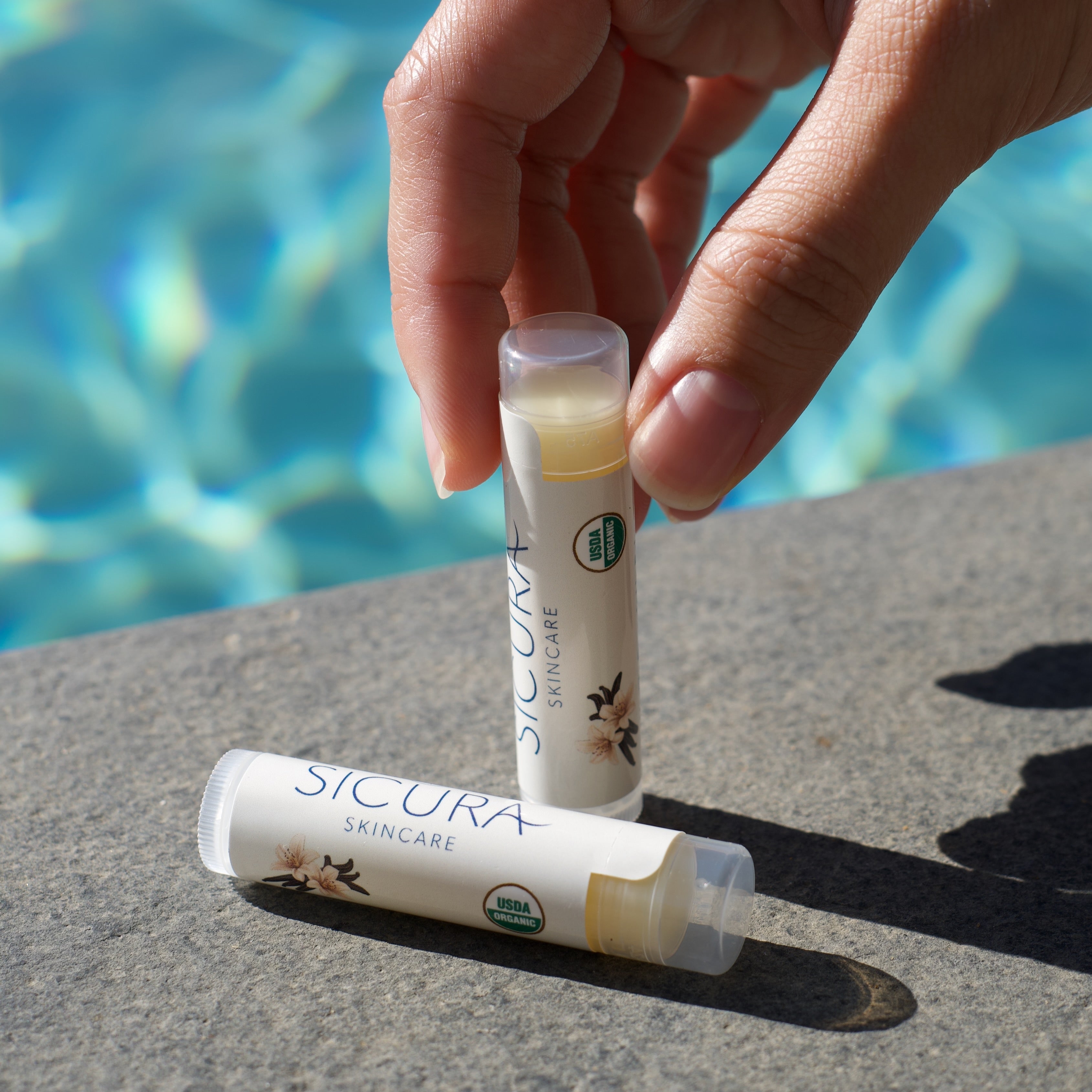 Hand holding a lip balm tube with a pool in the background