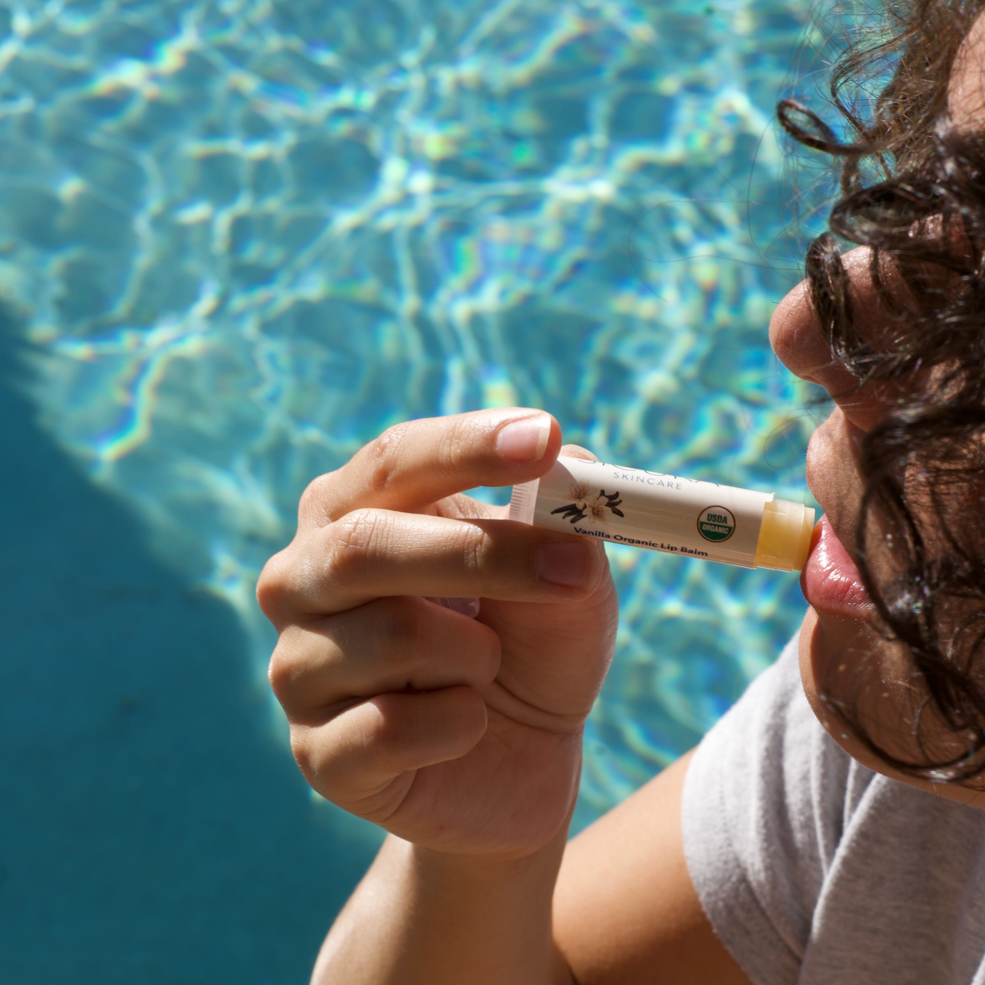 Person applying organic lip balm in front of a pool