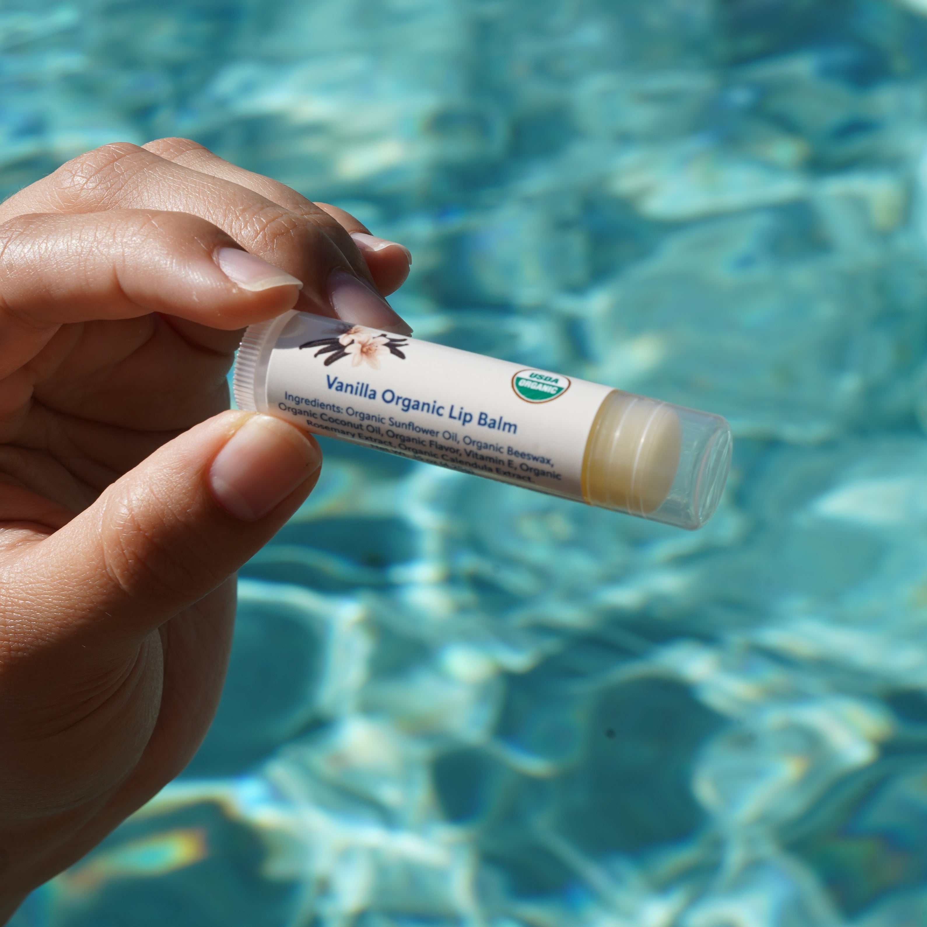 Hand holding a lip balm tube with a blurred pool background