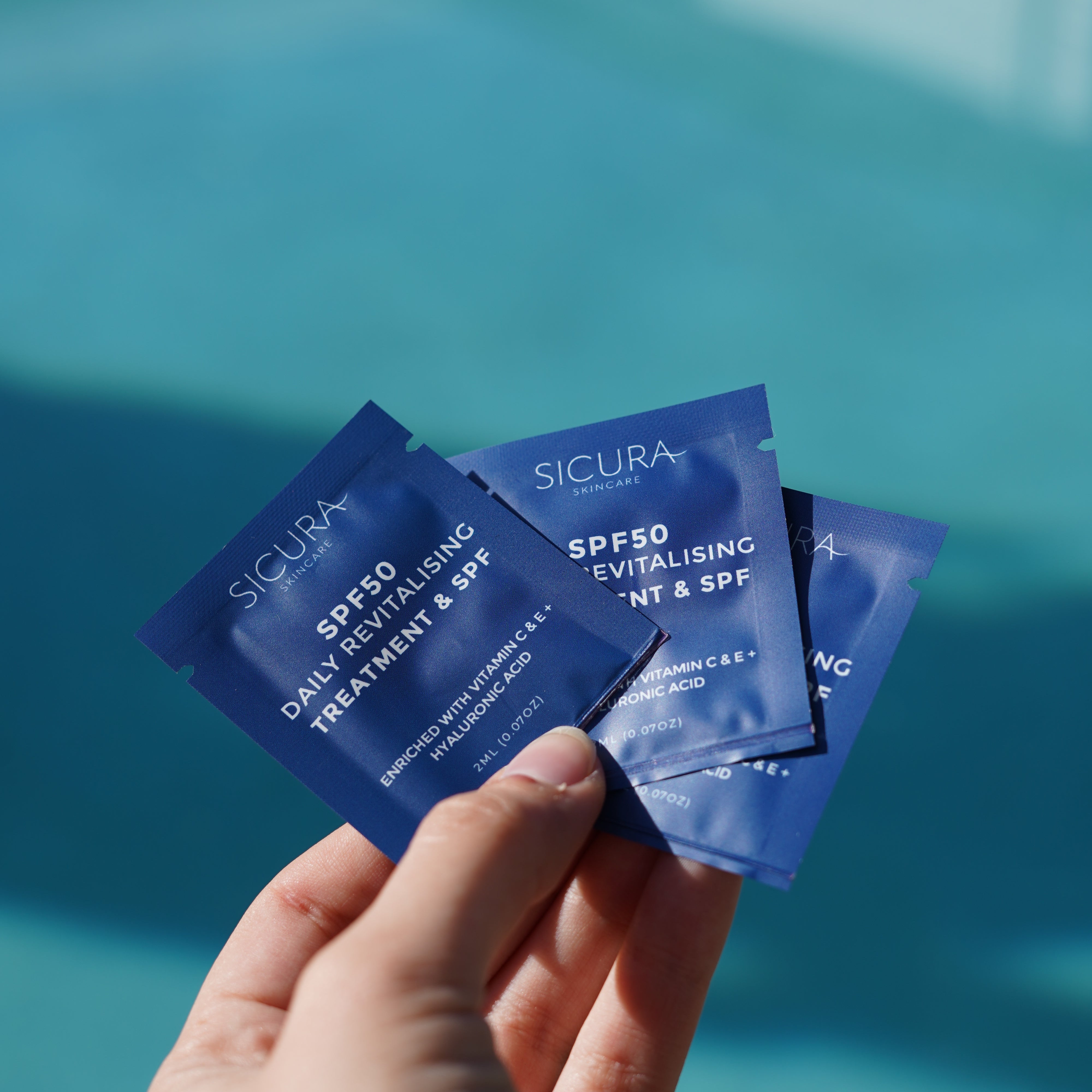 Hand holding blue skincare packets with 'Sicura' branding against a teal background