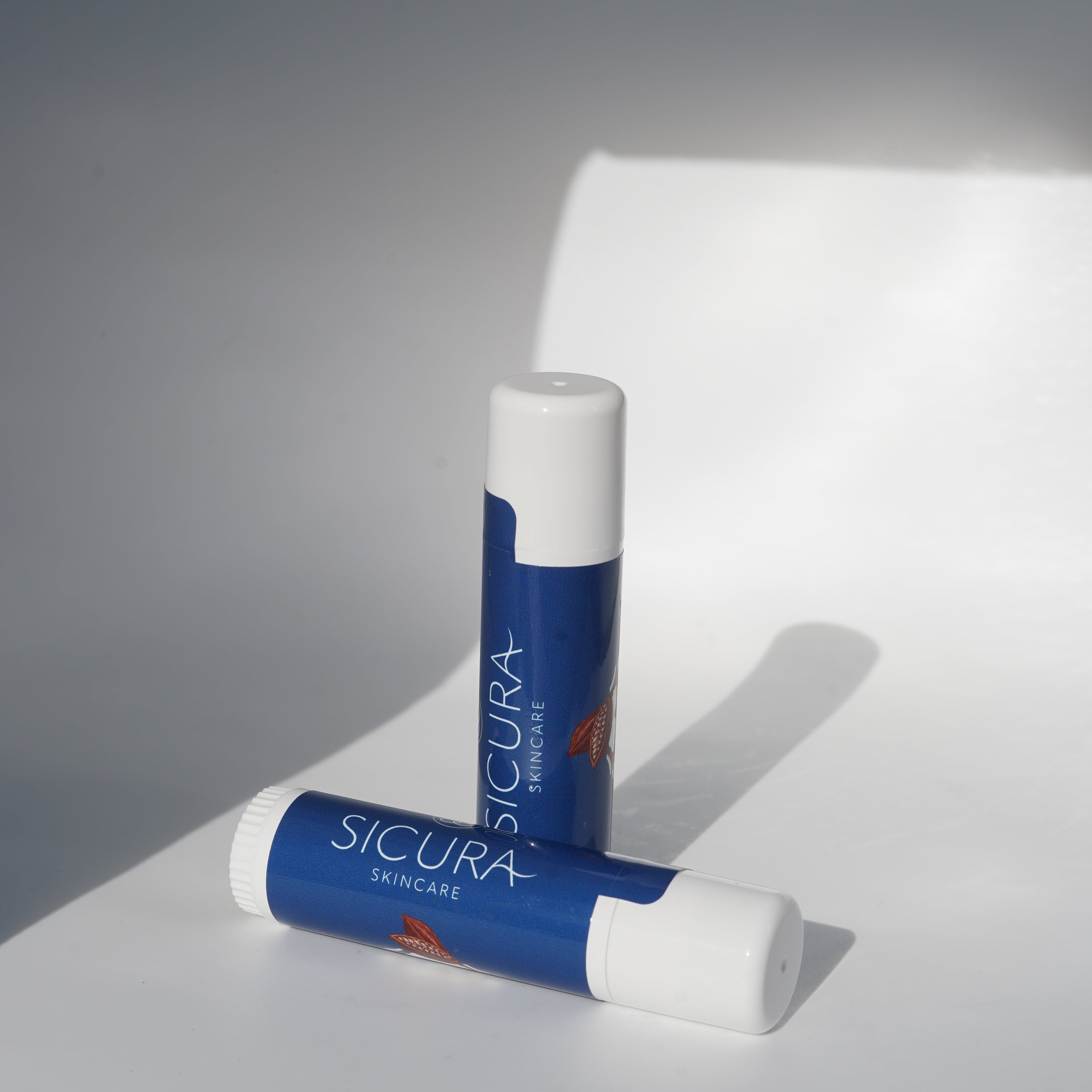 Two Scicura lip balms on a white surface with a gray background